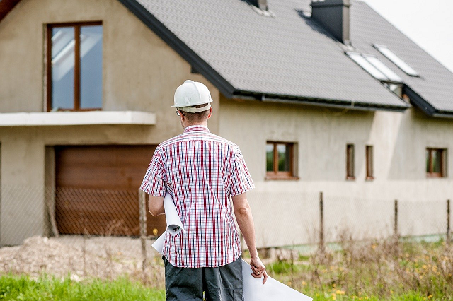 Stock image of a casually dressed architect in a hard hat, walking towards a new housing development.