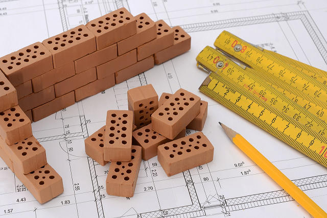 Stock image of bricks, measuring stick and a pencil on top of construction plans.